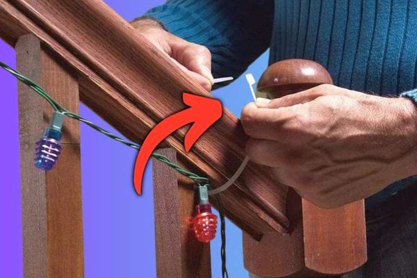 Un homme qui fixe une guirlande lumineuse à une balustrade en bois avec un collier de serrage en plastique.