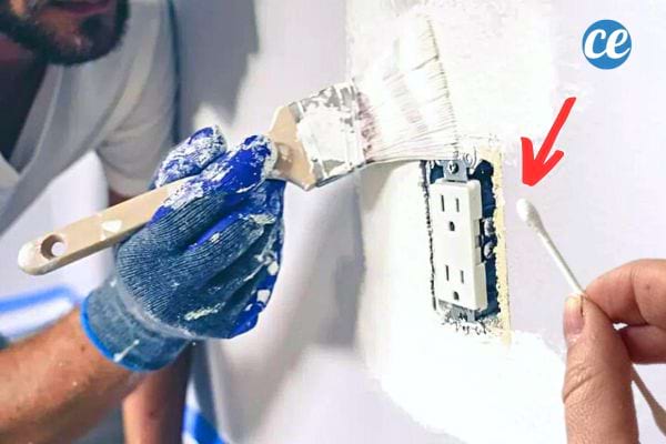 Un homme mettant de la peinture blanche autour d'une prise avec un coton-tige 