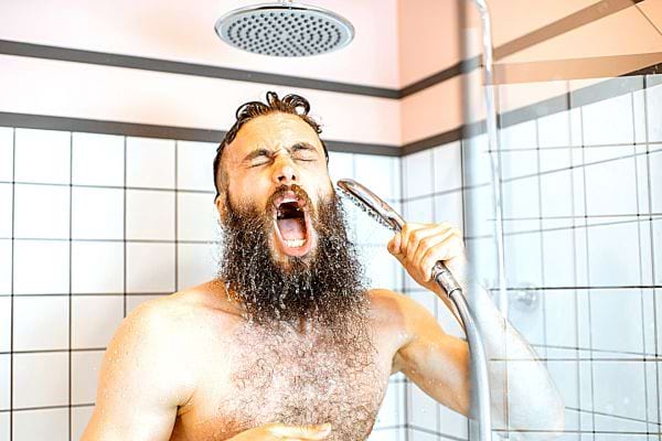 Un homme avec un air de souffrance qui a une grosse barbe sous la douche 