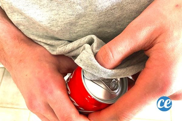 Une personne avec un tee-shirt gris qui essuie sa canette de Coca-Cola avec 