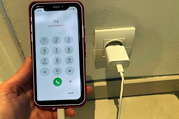 Une personne tenant un téléphone qui charge avec un numéro d'urgence sur l'écran