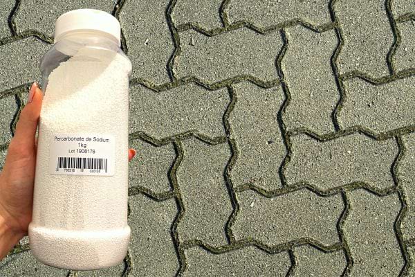 Une personne qui tient du percarbonate de soude au dessus de pavés autobloquants