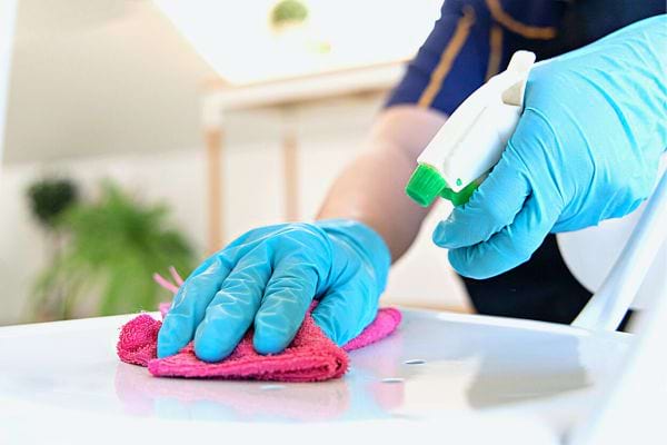 Une personne nettoyant avec un produit et des gants en latex bleus 