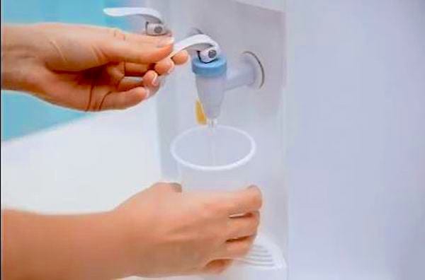 Une personne qui se sert de l'eau dans un gobelet à l'aide d'une machine à eau 