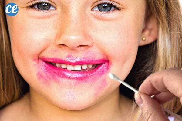 Une petite fille qui a du rouge à lèvre qui bave tout autour de sa bouche avec un coton-tige 
