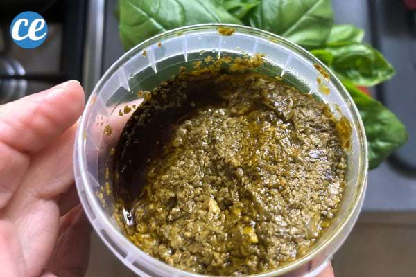 De la sauce basilic dans un pot en plastique tenu par une personne