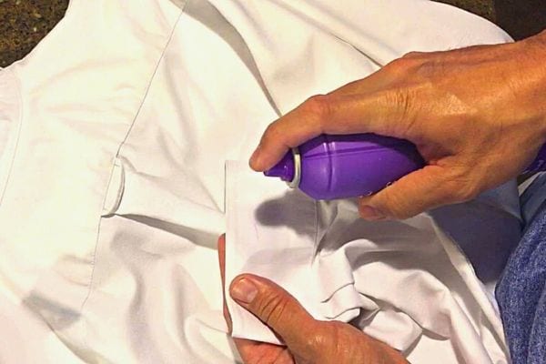 Une personne mettant un spray violet sur une chemise blanche 