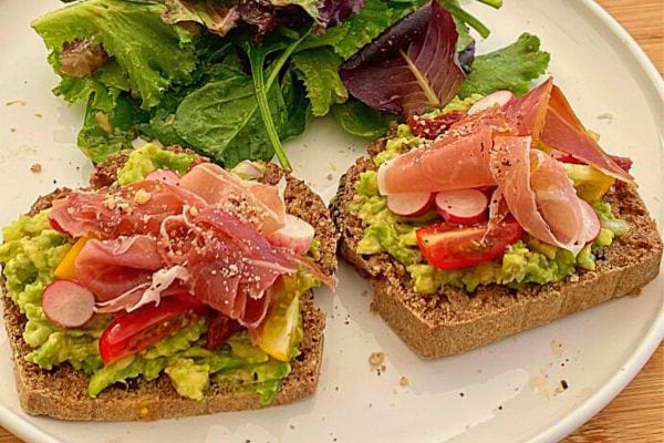 Deux tartines avocat, tomates et jambon cru dans une assiette avec de la salade