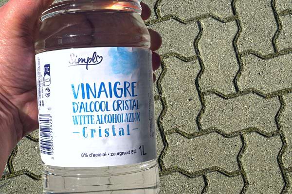 Une personne qui tient une bouteille de vinaigre blanc au dessus de pavés autobloquants