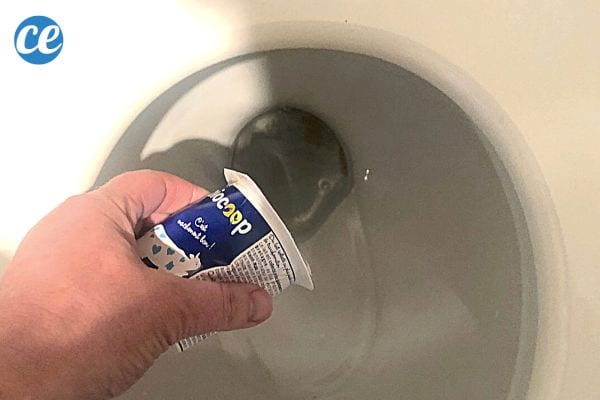 Une personne qui verse un pot de yaourt dans l'eau des toilettes 