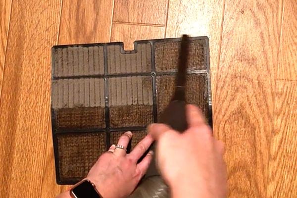 Un homme en train de passer l'aspirateur sur un filtre de climatiseur