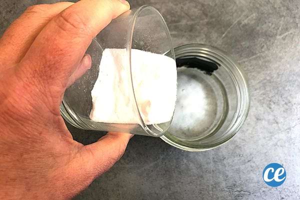 Une personne qui verse du bicarbonate dans un autre verre remplie d'eau 