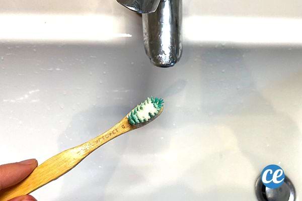 Du bicarbonate sur une brosse à dents en bois en dessous d'un robinet 