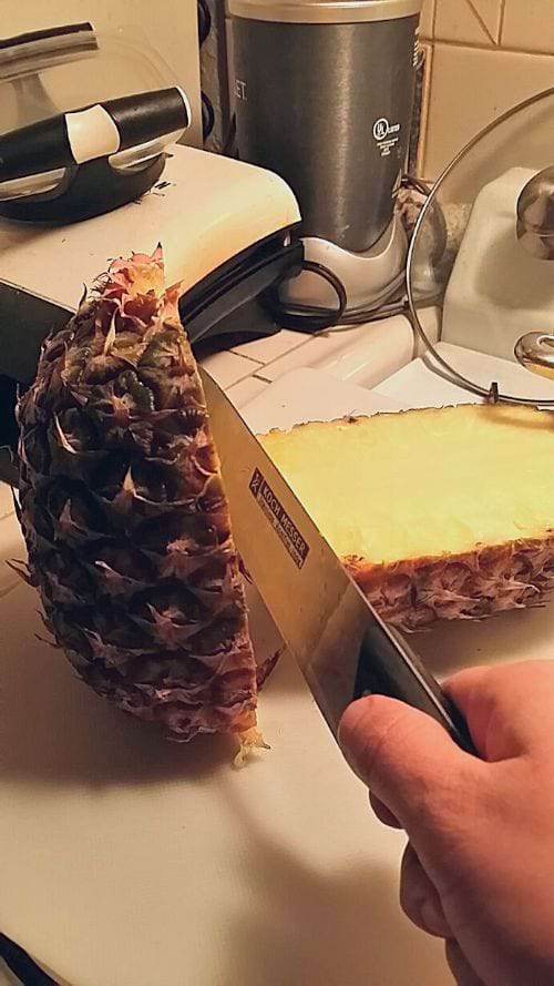 Une personne qui coupe la moitié d'un ananas