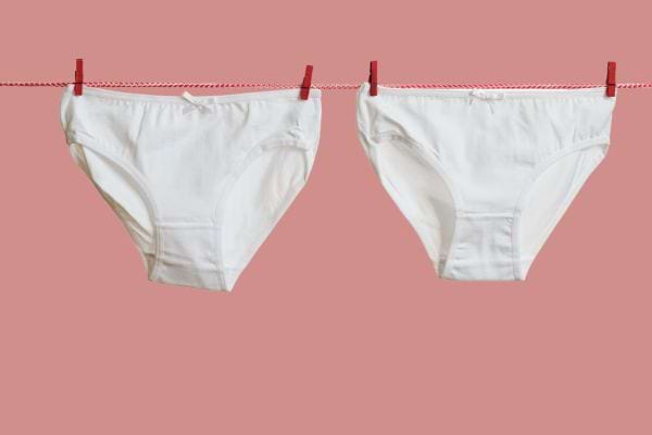 Deux culottes blanches qui sont suspendues à un fil avec des pincettes rouges 