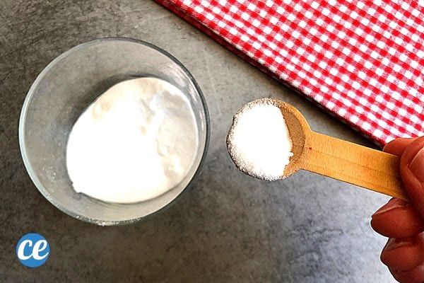 Une personne qui mets du bicarbonate dans un verre à l'aide d'un doseur en bois 
