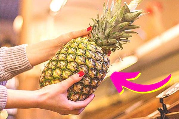Une femme avec du vernis rouge tenant un Ananas 