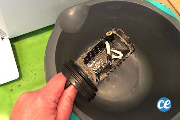 Une personne tenant le filtre de la machine à laver au dessus d'une bassine grise