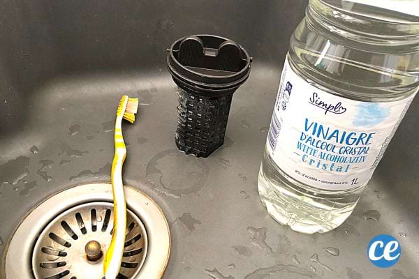 Un filtre de machine à laver dans un évier avec une brosse à dents et du vinaigre blanc