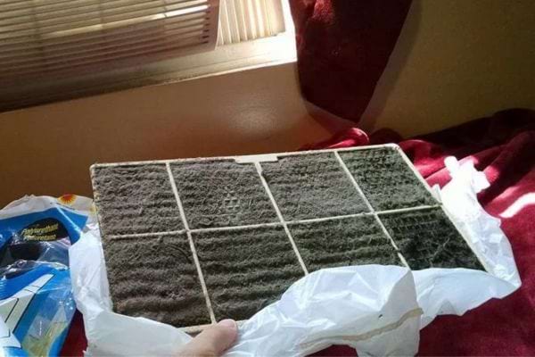 Une personne tenant un filtre de climatiseur remplie de poussière