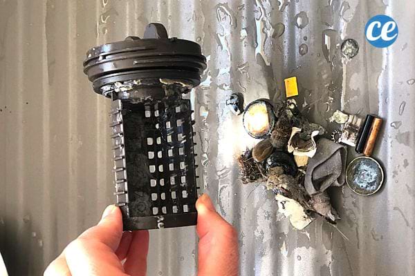 Une personne tenant un filtre de machine à laver avec toutes ses saletés