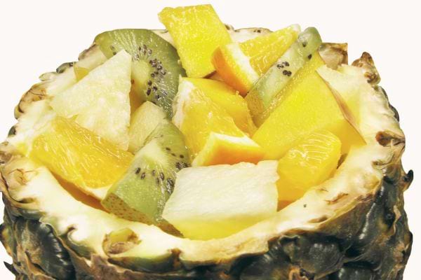 Des fruits coupés en petits morceaux dans un ananas dont des kiwis et de l'orange