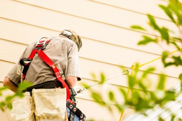 un homme accroché à un harnais sur un toit pour le nettoyer naturellement