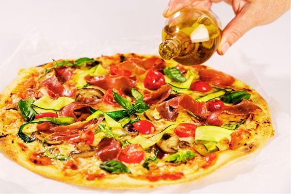 Une personne versant de l'huile sur une pizza 