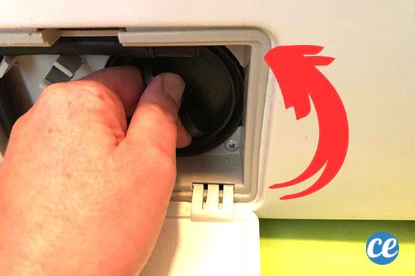 Une personne qui dévisse la porte du filtre de la machine à laver