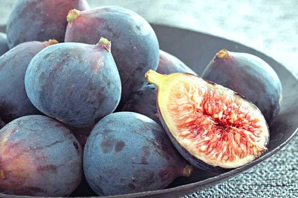 Plusieurs figues dont une ouverte à moitié dans une assiette