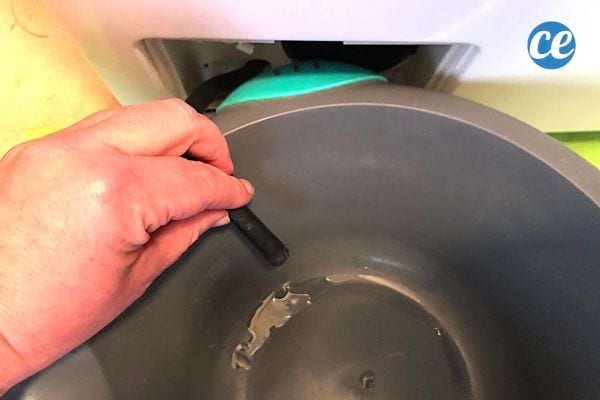 Une personne qui vide un filtre de machine à laver dans une grande bassine grise