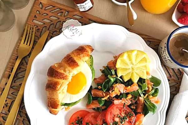 Une assiette blanche remplie de brunch avec un croissant salé et d'autres aliments