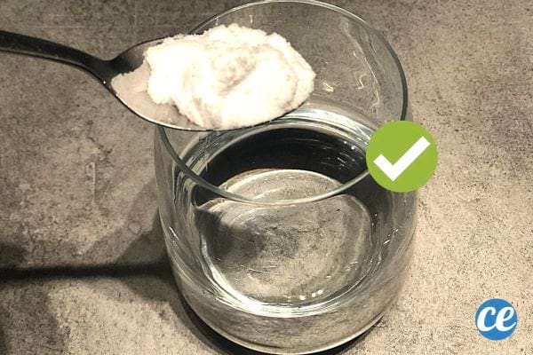 Une cuillère à café contenant du bicarbonate au dessus d'un verre d'eau pas entièrement remplie