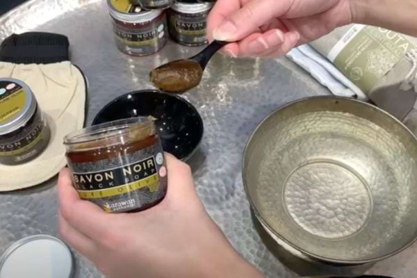 Une personne tenant une petite cuillère noir en plastique avec du savon noir dessus