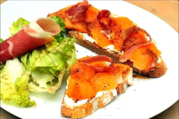 Une assiette blanche de tartine de melon, jambon et fromage frais