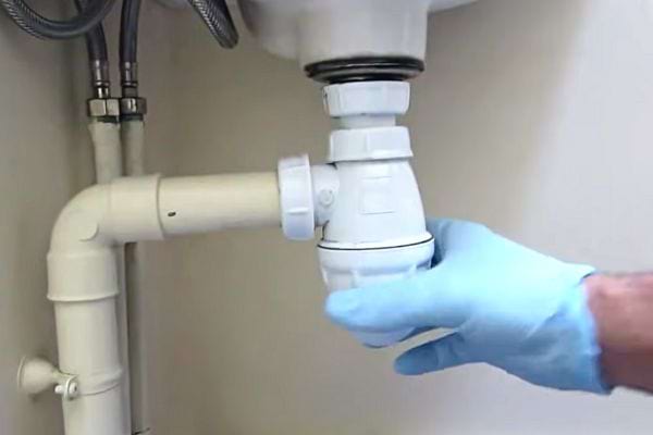 Une personne dévissant un siphon vêtu d'un gant en latex bleu