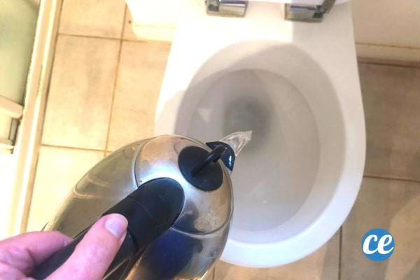 Une personne mettant de l'eau bouillante au fond des toilettes