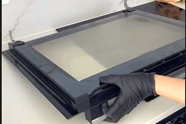 Une personne avec des gants en latex noir tenant la porte d'un four qui est enlevé