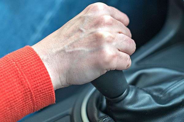 Eine Person, die ein orangefarbenes, langärmliges Oberteil trägt und ein Schaltgetriebe in der Hand hält