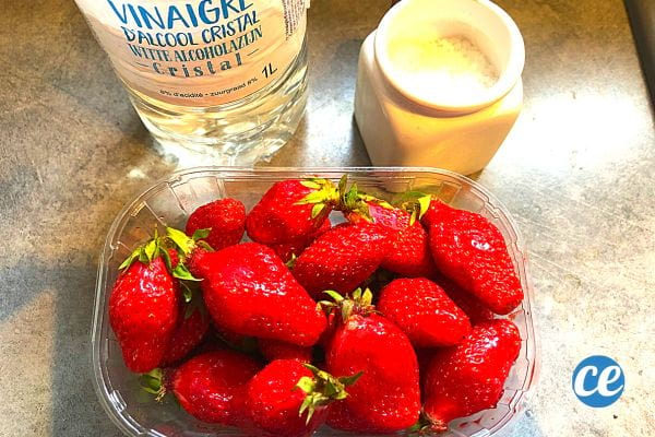 Strawberries in a tray with a bottle of white vinegar nearby 