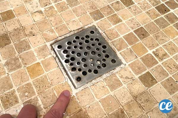 Une main dans une douche montrant une grille cimentée