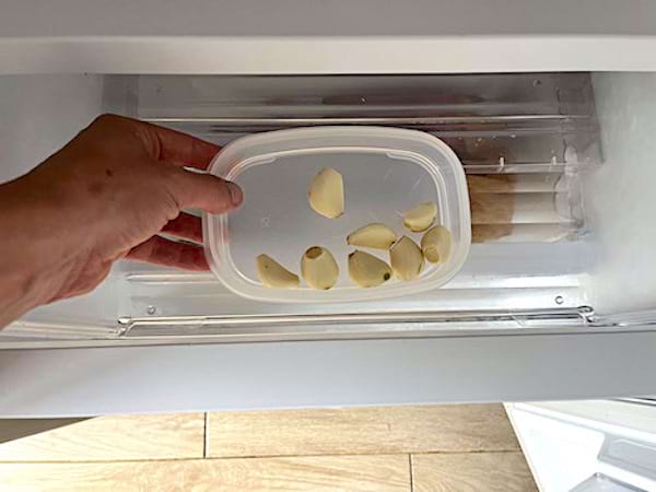 Une personne tenant une barquette en plastique contenant de l'ail dans un frigo 