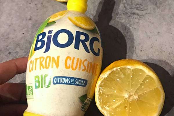 Une petite bouteille de jus de citron avec un citron découpé 