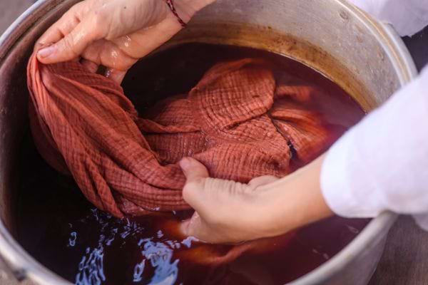Une personne mettant un linge marron dans de l'eau dans une grosse casserole