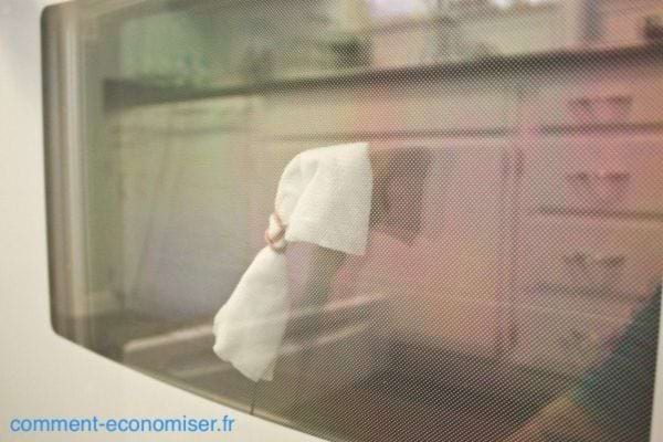 Une personne nettoyant la porte d'un four à l'aide d'un chiffon blanc 