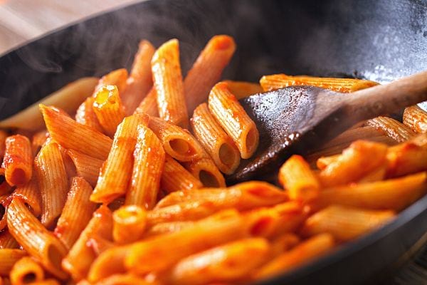Des pâtes dans une casserole et une cuillère en bois accompagnée de sauce tomate 