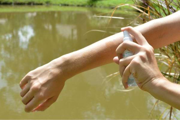 Une personne se mettant du répulsif à moustique sur le bras