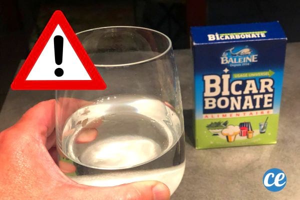 Une personne tenant un verre d'eau dans sa main avec un carton de bicarbonate de soude