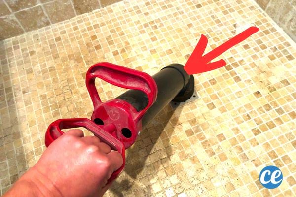 Une personne utilisant une pompe déboucheuse rouge dans une douche