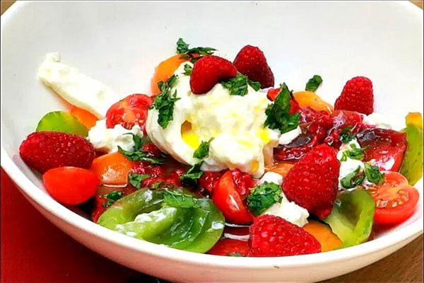 Une assiette blanche de salade de tomates, burrata et framboises